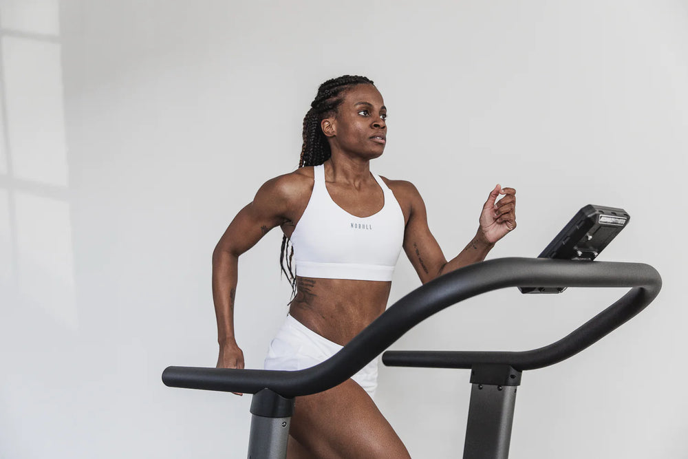 female athlete running on a treadmill wearing a white sports bra